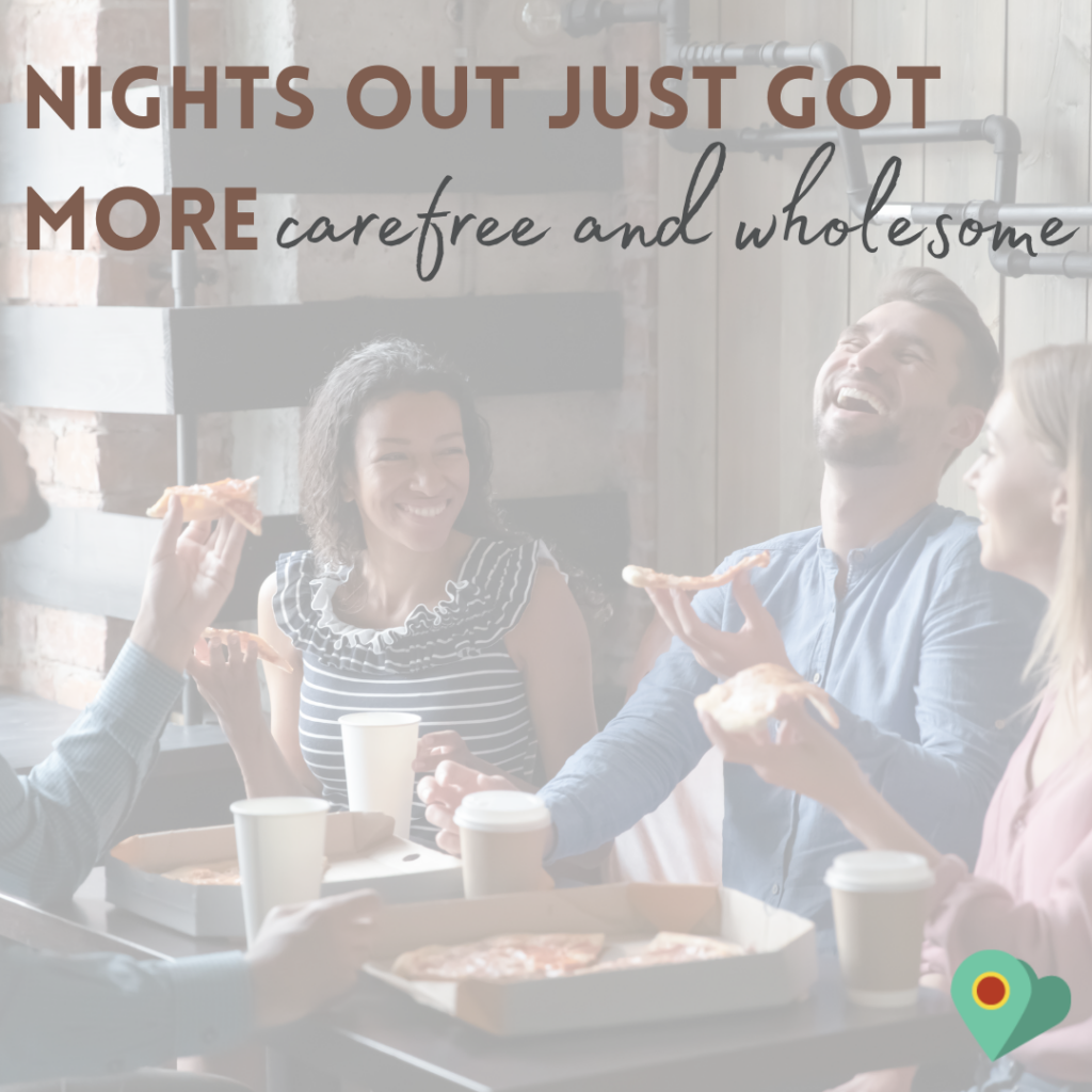 a group of friends sat around a brown table in what looks like a pub or restaurant setting. They are laughing with open smiles and look happy like they are enjoying themselves. There is food and drink on the table.