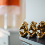 three ornaments of monkeys on a mantlepiece with a distorted lamp in the background - home photo.