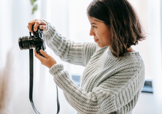 Woman holding a camera in both of her hands pointing it off in a direction as though taking a photo.